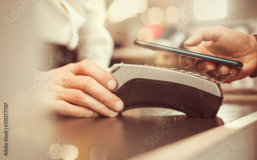 Customer hand pays with smartphone in store using NFC technology. Mobile phone paying the bill with contact less technology.