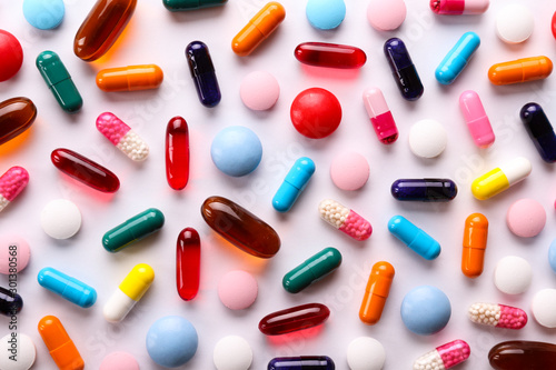 Flat lay composition with bunch of different colorful pills in scattered all over the table. Pile of opened medication on paper textured background. Close up, copy space.