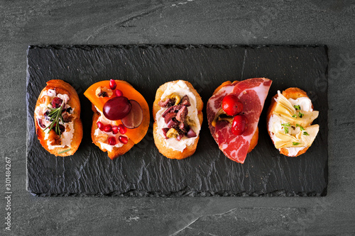 Mixed crostini appetizers with a variety of toppings. Top view on a dark slate background. Party food concept.