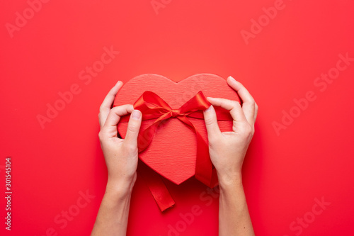 Close up on female hands holding a gift in a pink heart presents for valentine day, birthday, mother's day. Flat lay. Symbol of love. Valentines day background with a gift boxes on concrete board.