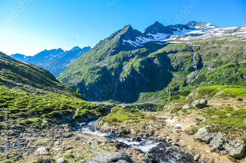 A serene view on snowy mountain from a small stream's side. The stream starts it's long way to the sea. Tall glacier towering above the landscape. Spring in the alpine valley.