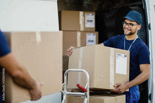 Happy manual worker unloading cardboard boxes from delivery van.