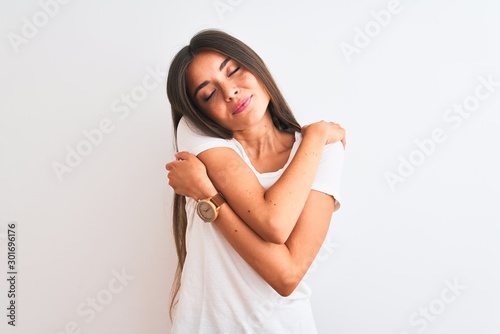 Young beautiful woman wearing casual t-shirt standing over isolated white background Hugging oneself happy and positive, smiling confident. Self love and self care