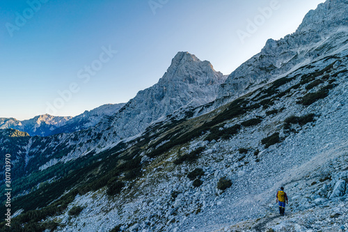 A hiker or climber walking in an alpine mountain landscape. Trekking with a backpack. Sunset in the mountains, hiking in the alps. Silhouette of a hiker. Rocky path in the austrian alps.