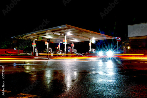 Gas station at night with lights from passing cars as people fill up with petrol