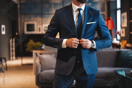 Handsome man adjusting his jacket while standing in modern office.