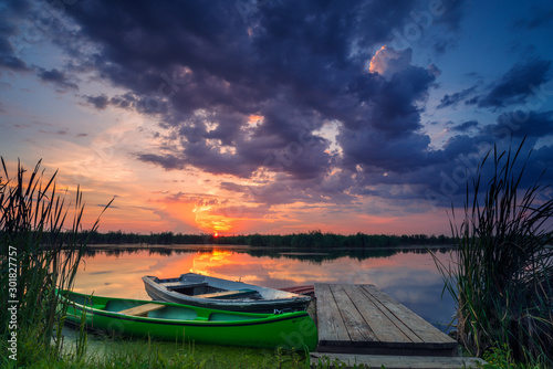 Two boats on a lake near a pontoon at sunrise with dramatic clouds