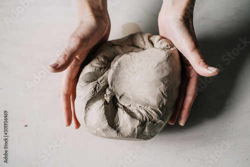 Female potter hands working with clay in workshop. White desk on background