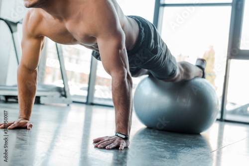 cropped view of handsome sportsman doing plank on fitness ball in sports center