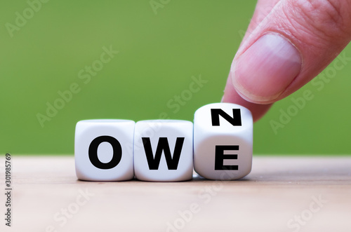 Hand turns a dice and changes the word "owe" to "own".