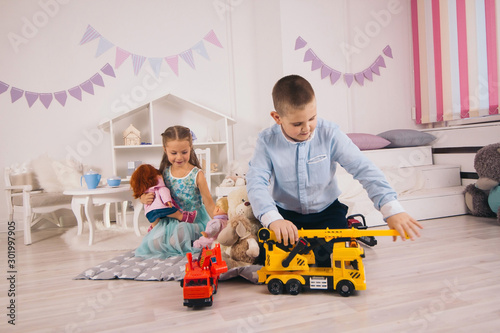 beautiful happy caucasian children playing in their room, boy playing with cars, girl playing with dolls