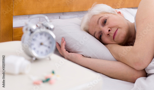 Upset senior ledy with sleep disorder lying in bed