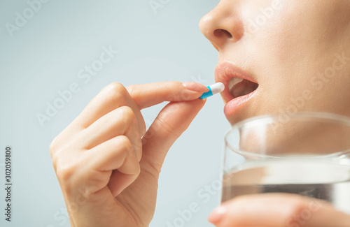 Woman taking a medication capsule or vitamin with glass of water.