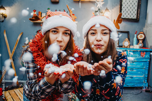 Two girlfriends in santa hats play with snow