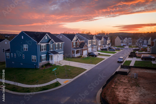 Aerial view of quiet modern colonial single family home with blue vinyl siding on a neighborhood street with a dead end cul de sac during a stunning sunset