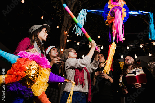 Mexican Posada friends breaking a Piñata celebrating Christmas Mexico