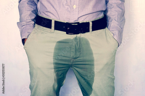 A man standing in wet pants against the wall. Urinary incontinence is an increasingly popular disease affecting younger males. incontinence and wet pants. a dark spot on a light trousers.