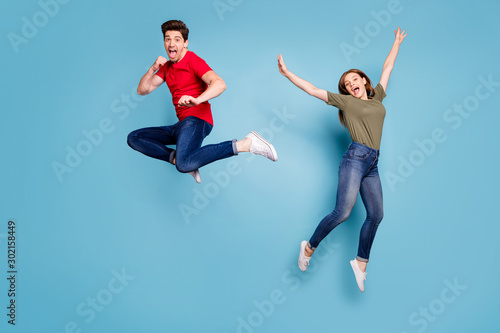 Full size photo of funky crazy two people spouses students man fight kick hands fists woman jump fool raise arms wear green red t-shirt denim jeans sneakers isolated blue color background