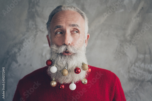 Closeup photo of funny white haired old man with colorful toy balls in long beard looking silly side empty space wear stylish red pullover isolated grey color wall background