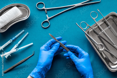 Preparing for plastic surgery. Doctor's hands takes scalpel on blue background with surgical tools top view