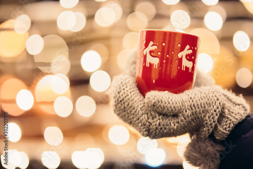 Christmas light and a woman holding in hand a red mug with hot drink