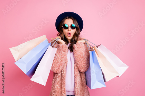 Photo of pretty millennial lady carry many packs shopper tourism abroad look unbelievable sales low prices mall wear fluffy jacket sun specs blue hat isolated pink background