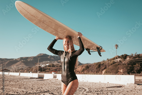 young woman standing with surfboard at Malibu beach. california lifestyle