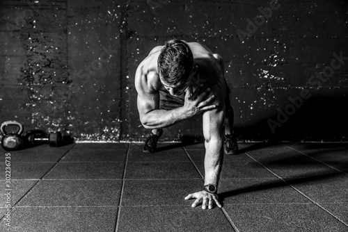 Young sweaty strong and fit muscular man push ups workout with touching his shoulder on one hand in the gym on the floor cross training black and white real people