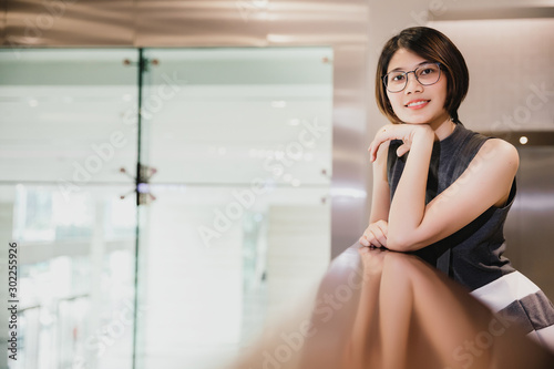 Portrait of Asian young short hair beautiful woman wearing glasses and grey dress looking at camera posing with hand on chin
