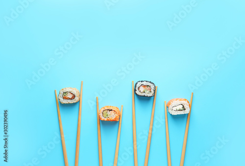 Tasty sushi rolls and chopsticks on color background