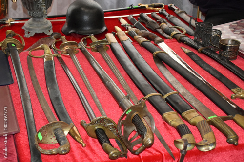 Many sabers, swords, spaces and daggers with helmet exhibited on red textile