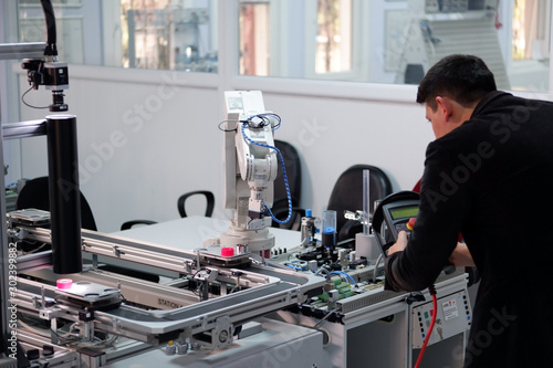 industry 4.0 concept: Man (engineer) is programming robotic arm with control panel (teach pendant) on smart factory production line background. Selective Focus.