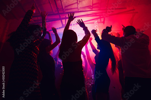 Team. A crowd of people in silhouette raises their hands on dancefloor on neon light background. Night life, club, music, dance, motion, youth. Purple-pink colors and moving girls and boys.