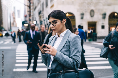 Hispanic female entrepreneur dressed in formal jacket making online communication on website typing sms answer via smartphone gadget, intelligent young woman using 4g wireless on cellphone device