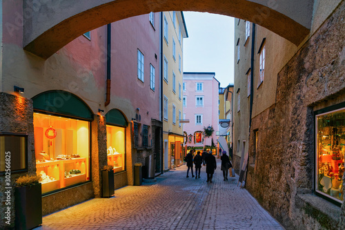 People at Narrow Street with shops and stores at Old city of Salzburg, Austria. Building architecture of Mozart town, Europe, winter. Panorama and landmark. Cityscape in Evening. Travel and tourism.