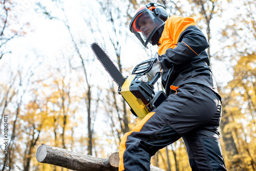 Professional lumberjack in protective workwear working with a chainsaw in the forest. Woodcutter makes a logging outdoors