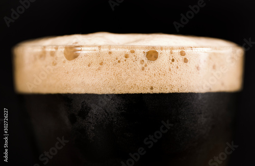 Glass of dark beer isolated on black background. Foam close up.