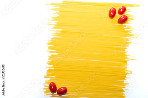 Dry spaghetti on a white background. Cherry tomatoes on a yellow pasta background. Italian pasta. Copy space