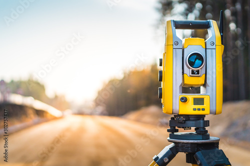 Surveyors equipment (theodolite or total positioning station) on the construction site of the road or building with construction machinery background