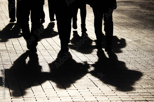 Silhouettes and shadows of people on the city street. Crowd walking down on sidewalk, concept of strangers, crime, society, gang or population