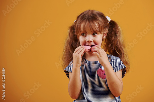 Cute little girl with sweet food in the studio against yellow background