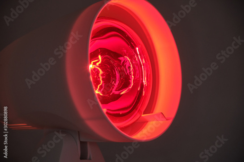 Close up of infrared lamp glowing in the dark with its warming red light to cure for example colds or tensions.