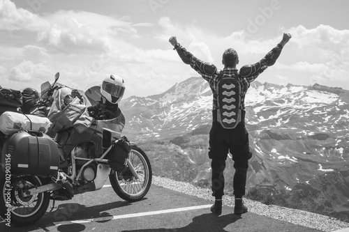 A back view motorcycle traveler is happy arrived at his destination. Conquering the top of the mountain, Grossglockner pass, biker dressed in a protective jacket armor black and white. Austria