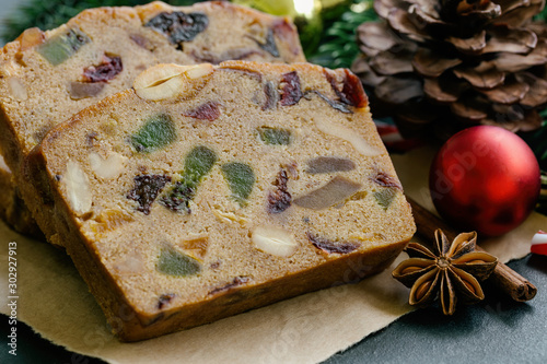 Sweet fruit cake slices on brown paper put on black granite table in close up view with Christmas decoration. Traditional rum fruit cake for Christmas celebrate festival. Homemade bakery concept.