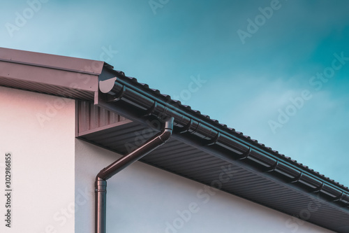 Chocolate-colored plastic gutter on the roof of the building and downpipe on the wall