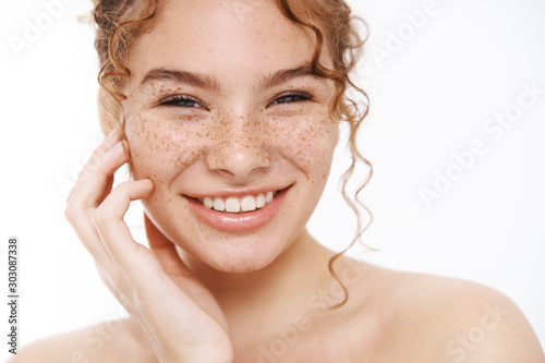 Headshot happy tender redhead girl freckles smiling broadly white teeth standing naked gently touching cheek taking care body showering, applying skincare cosmetics treatment, daily hygiene procedure