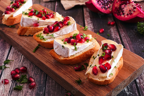 Holiday crostini appetizers with brie cheese, pomegranates and parsley. Close up on a serving board against a rustic wood background. Party food concept.