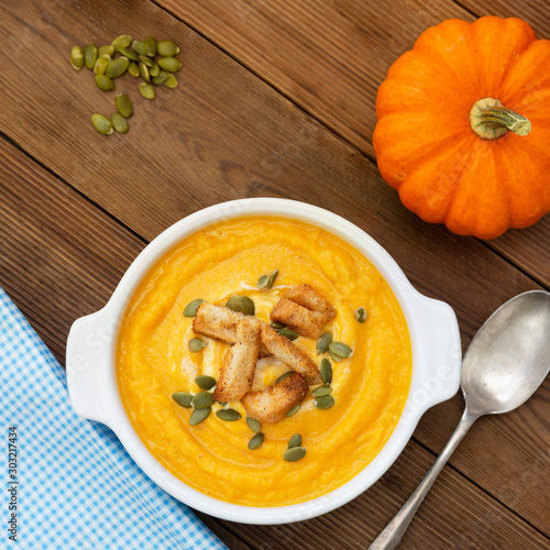 Pumpkin soup in a bowl,with fresh pumpkin seeds. Autumn foods. Healthy, vegetarian food, wooden background. Square image.