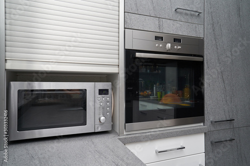 Metallic microwave and oven in gray kitchen interior