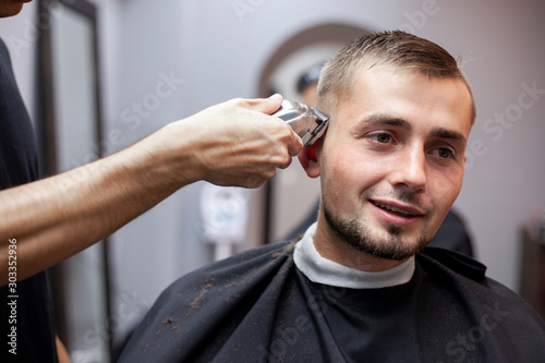 young guy makes a short haircut in a barbershop with a trimmer, close-up